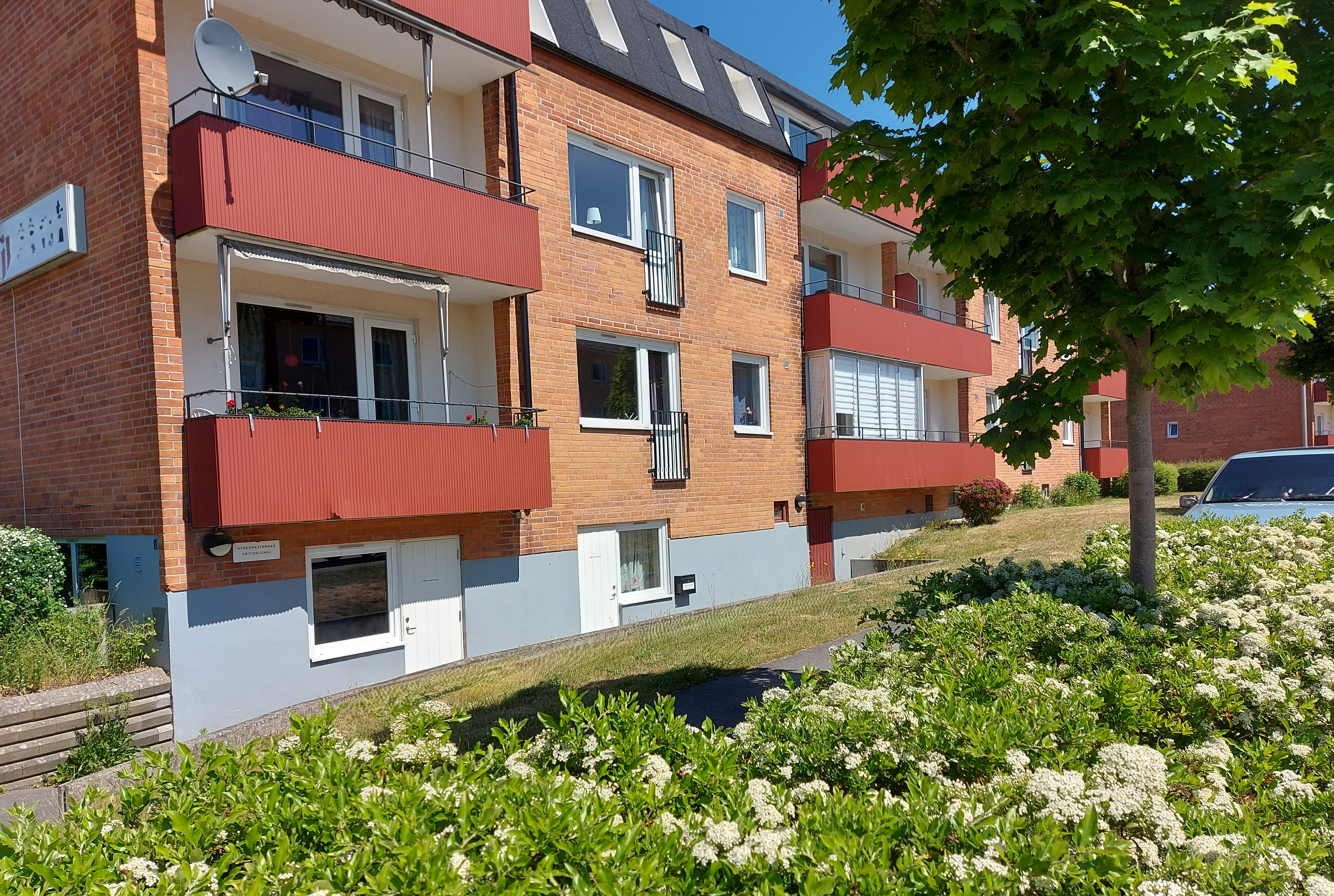 Bild på baksidan av ett rött tegelhus. Där finns röda balkonger och i förgrunden gräsmatta 